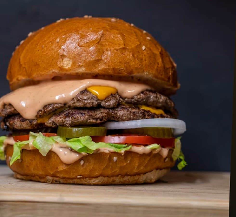 A double smash burger, stacked high on a wooden board